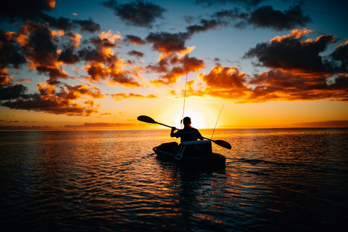 Kayak angler silhouetted against a dramatic sunset sky with fishing rod