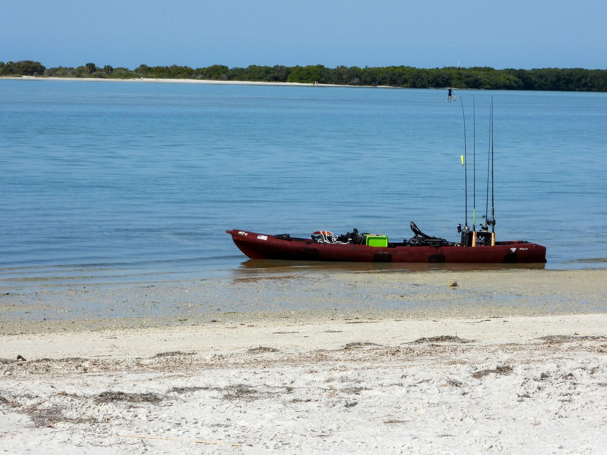Fully rigged fishing kayak with multiple rod holders and gear setup beached on sand